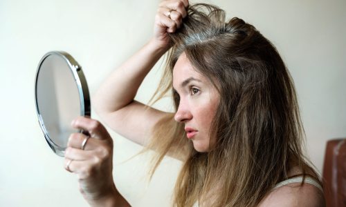 Young woman looks in the mirror at her gray hair roots. Problem of gray hair and loss hair